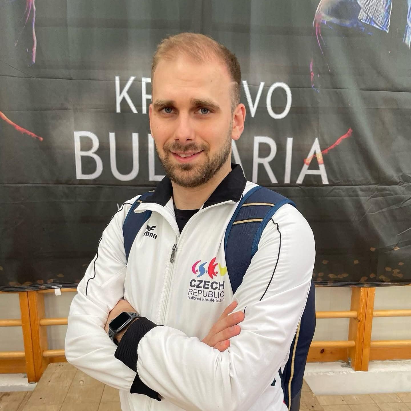 Person wearing Czech Republic karate team jacket, standing with crossed arms.