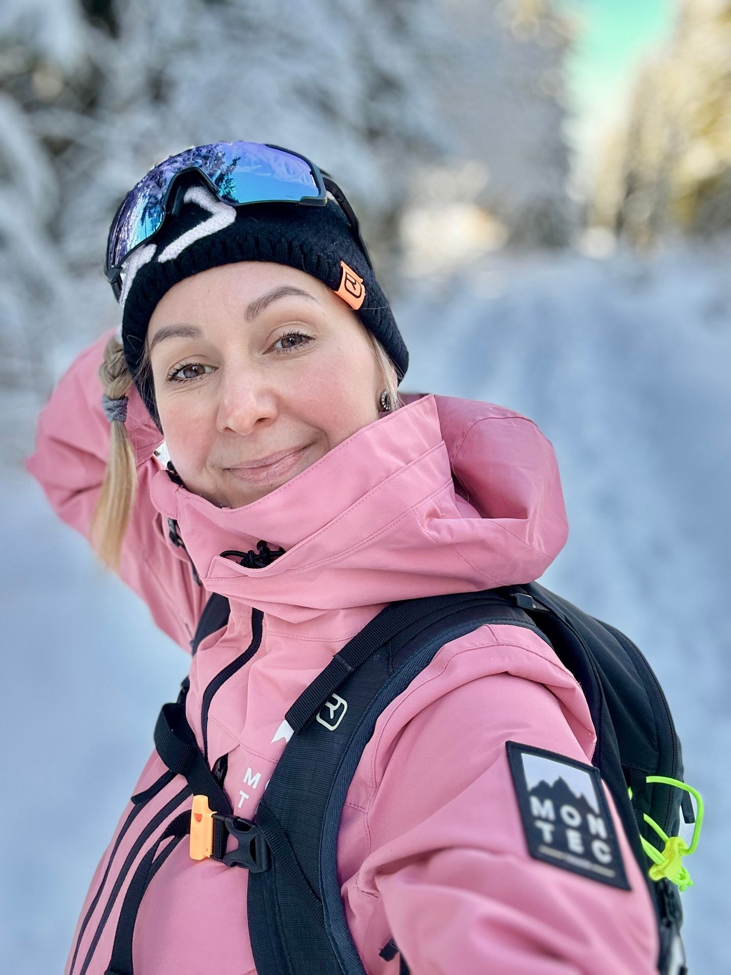 Person in pink winter jacket and hat, wearing ski goggles, standing in a snowy outdoor setting.